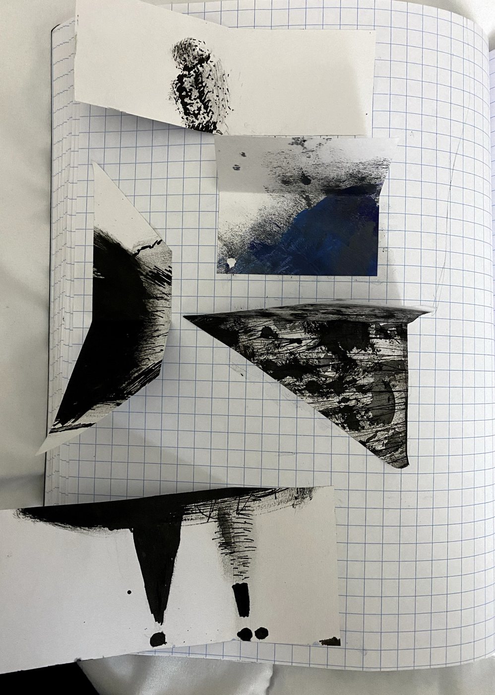 Notebook page holding cut pieces of the ink figure: the bun, the skirt's dark edge, and the legs, set apart with pieces of blue and black wash.