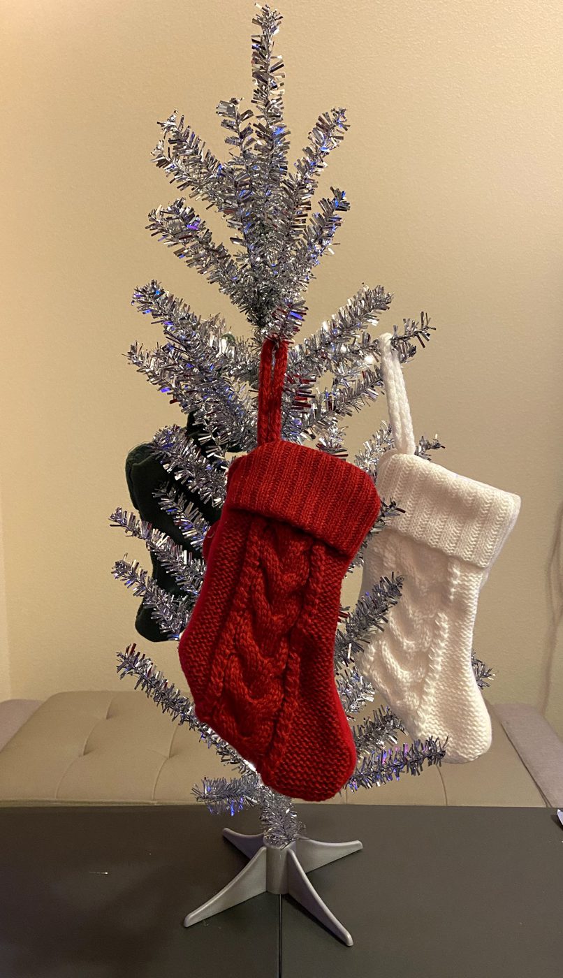 Photograph of a small silver tinsel tree holding a red, a white, and a dark knitted stocking.