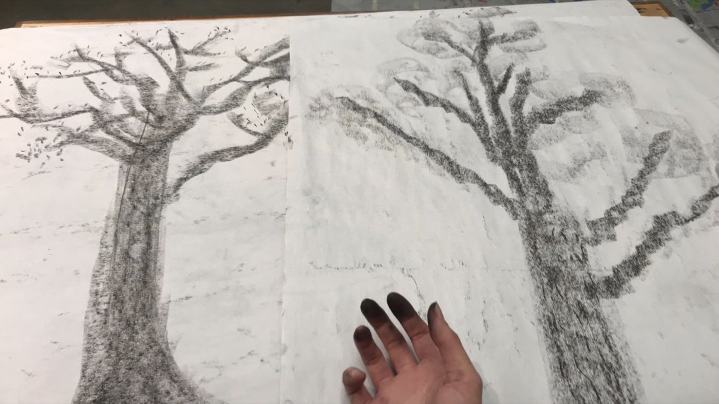 Two large charcoal trees on adjoining sheets, with a charcoal-blackened hand resting at the bottom edge.